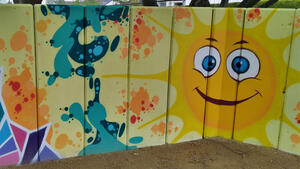 Wand, bemahlt mit Graffitis und einer lächelnden Sonne.