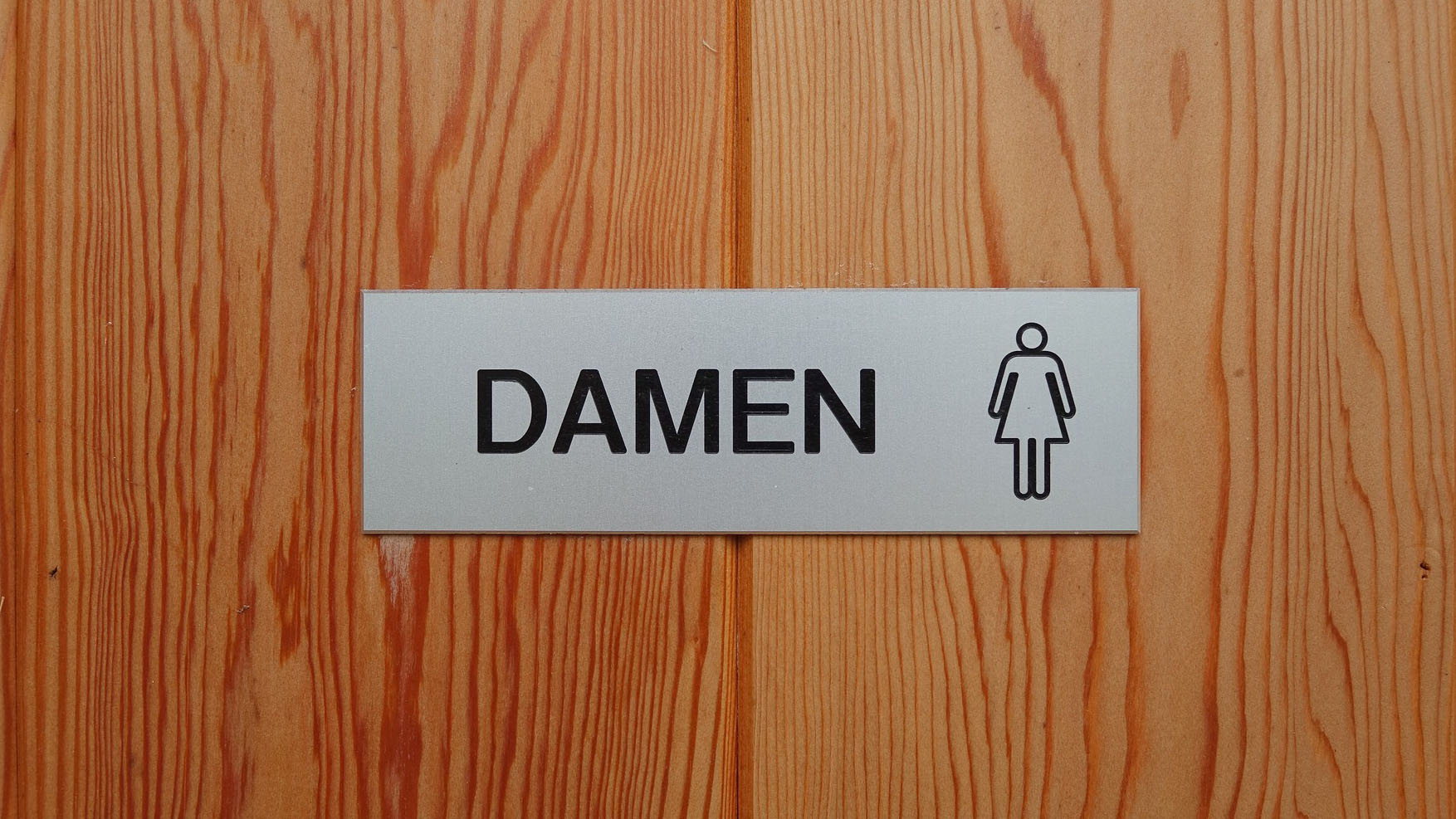 Holztür mti dem Schild "Damen" und einem Piktogram einer Frau.