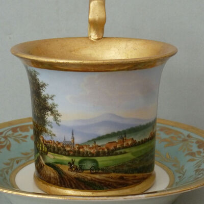 Eine Fürstenberger Tasse ist rundum mit einer Ansicht der Stadt Wolfenbüttel bemalt. Innen ist die Tasse vergoldet.