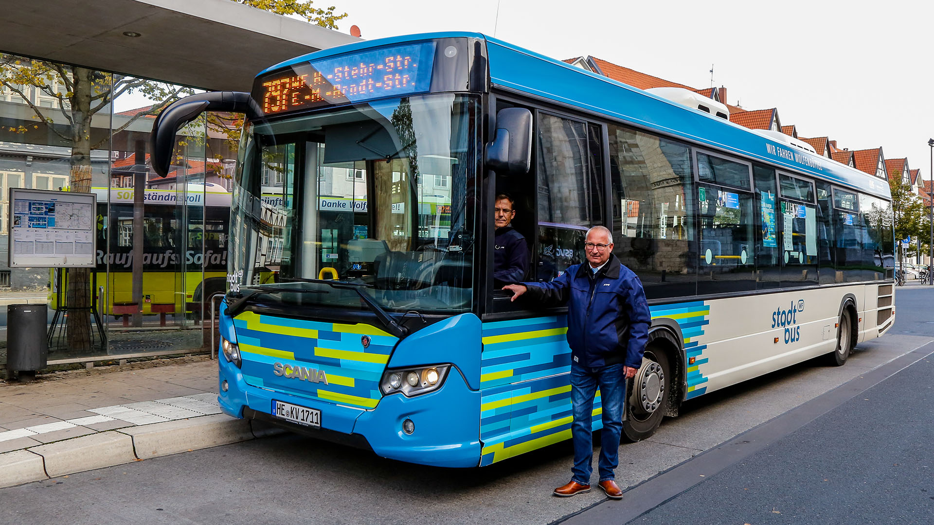 Ein Bus in dem neuen Design des Stadtbusses WF. Ein Busfahrer sitzt hinter dem Steuer, ein Kollege steht neben dem Bus am offenen Fahrerfenster.