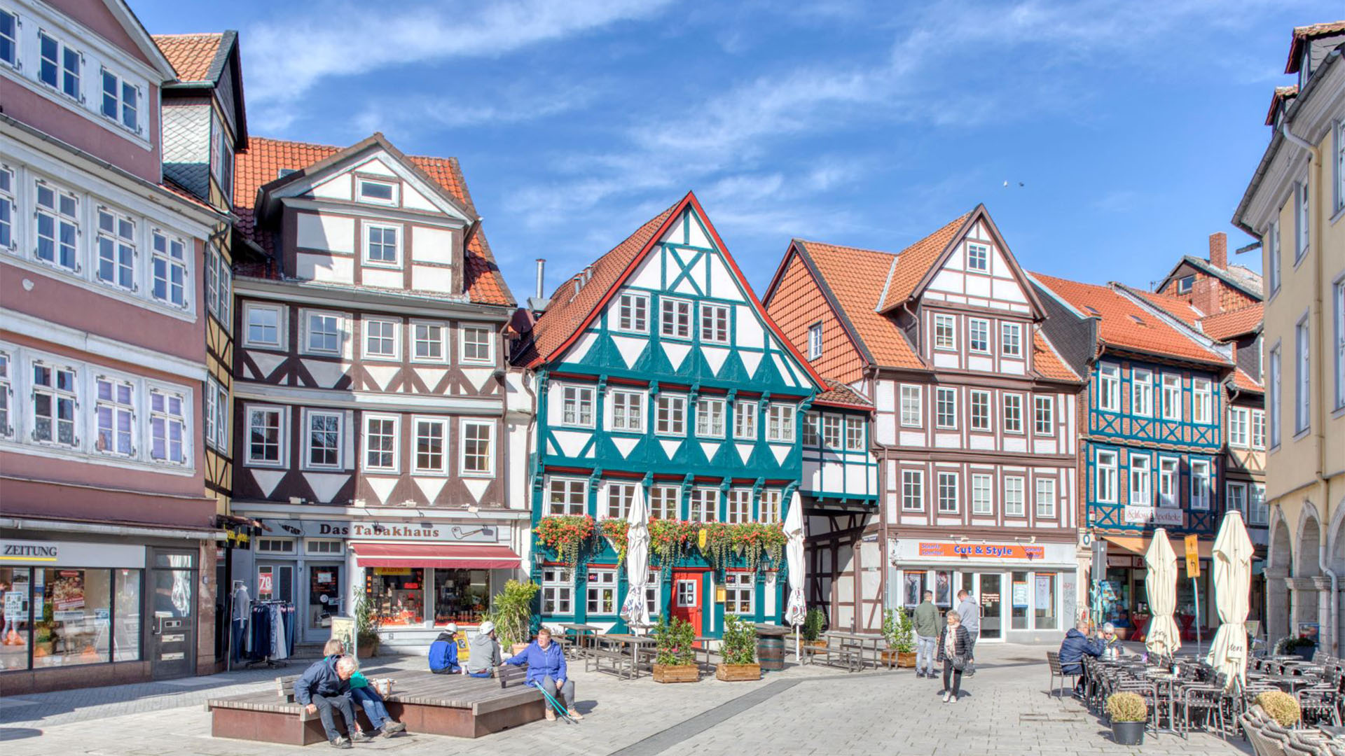 Blick in die Wolfenbütteler Fußgängerzone mit Fachwerkhäusern und Sitzgelegenheiten, auf denen sich Bürgerinnen und Bürger ausruhen.