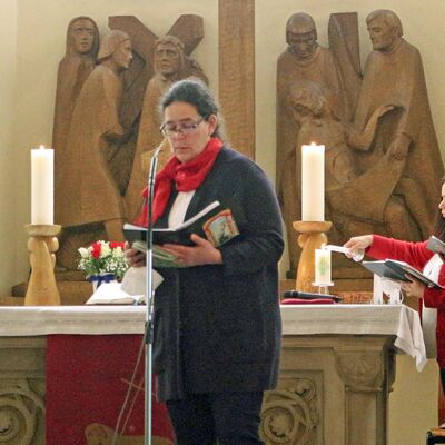 Eine Frau steht vor einem Altar und hält eine Lesung. Auf dem Altar sind zwei große Kerzen zu sehen.