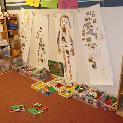 Eine aufgeräumte Spielecke mit Holzregalen und Kisten gefüllt mit Bausteinen und Spielzeug.