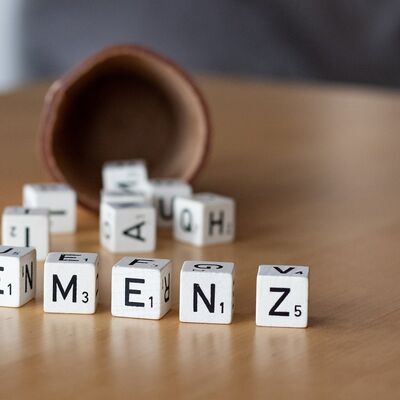 Auf einer Tischplatte liegen vor einem Würfelbecher mehrere Buchstabenwürfel. Einige davon bilden das Wort "Demenz".