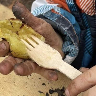 Eine schmutzige Kinderhand hält eine gekochte Kartoffel. Mit der anderen Hand sticht eine Gabel hinein.