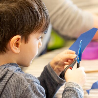 Ein Kind schneidet mit einer Schere blaues Papier.