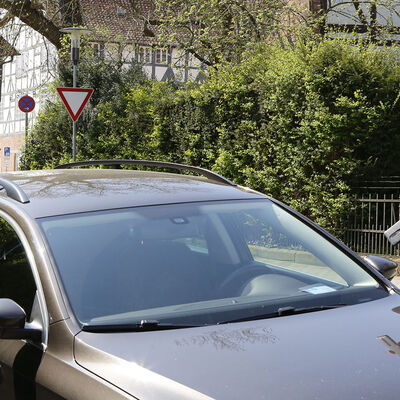 Ein Mann und ein Schüler kontrollieren bei einem geparkten Auto den Parkschein.