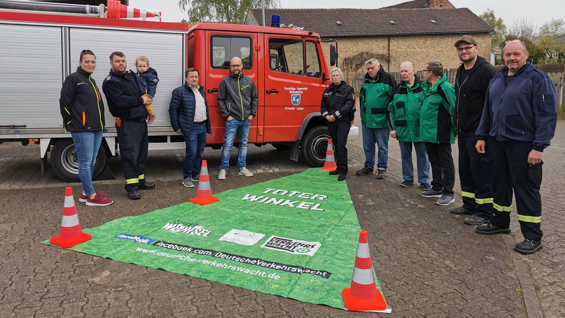 Gruppenbild mit elf Personen vor einem Feuerwehrfahrzeug. Davor liegt ein grünes Dreieck mit der Aufschrift "Toter Winkel".