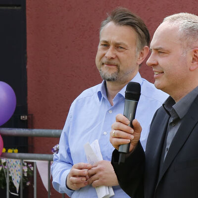 Porträt zweier Männer, einer hält ein Mikrofon.