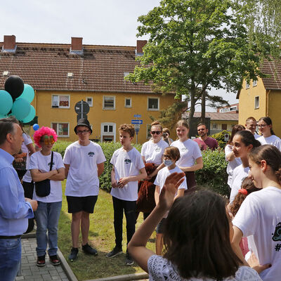 Bürgermeister Ivica Lukanic spricht vor einem Haus zu einer Gruppe Jugendlichen mit Add.Lantis-T-Shirts