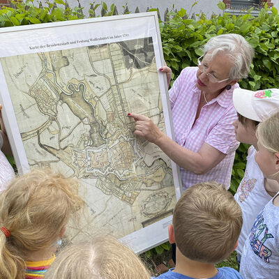 Eine Frau zeigt Kindern eine alte Stadtkarte.