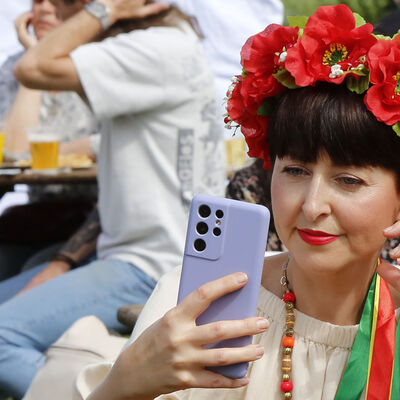 Eine Besucherin mit Blumenkranz inden Haaren fotografiert mit ihrem Smartphone beim Ukraine-Fest am Fümmelsee