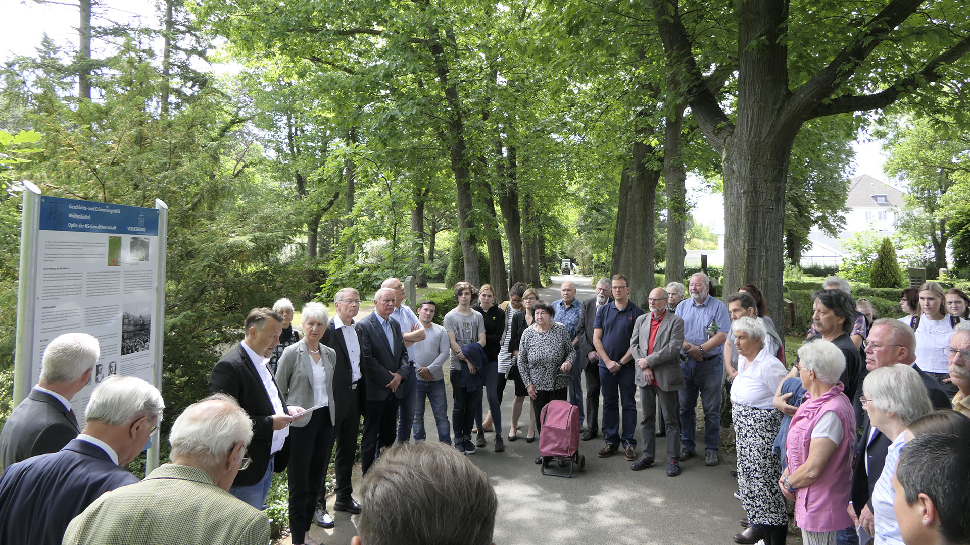 Auf dem Friedhof stehen viele Menschen rund um eine große Informationstafel, vor der ein Mann spricht. Es ist die Geschichts- und Erinnerungstafel Wolfenbüttel: Opfer der NS-Gewaltherrschaft