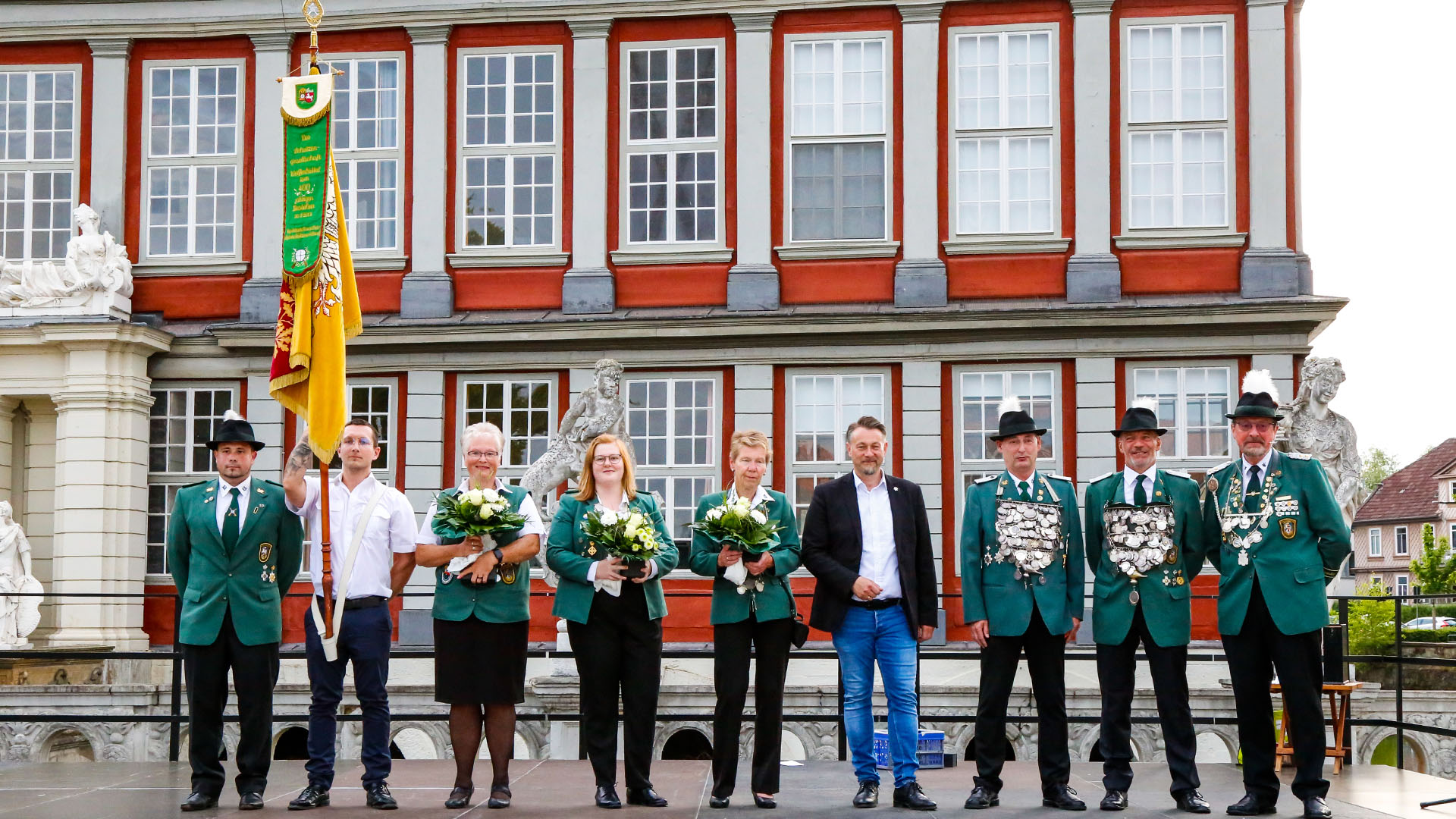 Vor dem Wolfenbütteler Schloss steht der Bürgermeister mit acht Männern und Frauen in Schützenuniform und Fahne.