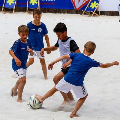 Mehrere Kinder spielen Fußball im Sand.