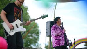 Ein Gitarrist und ein Sänger in einem lilafarbenem Jacket stehen auf einer Bühne.