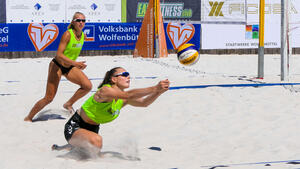 Zwei Frauen in grünen Trikots spielen mit einem Ball im Sand.