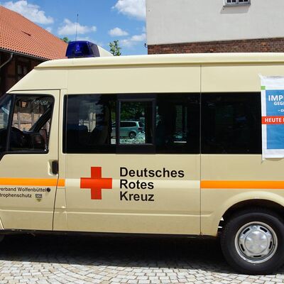 Kleinbus vom Deutschen Roten Kreuz mit einem Plakat mit Hinweisen zur Impfaktion gegen Covid-19 "Ohne Termin" und "heute hier".