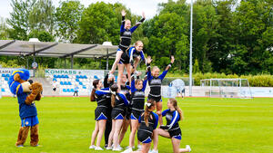 Cheerleader in blau/schwarzen Trikots stehen aufeinander als menschliche Pyramide.