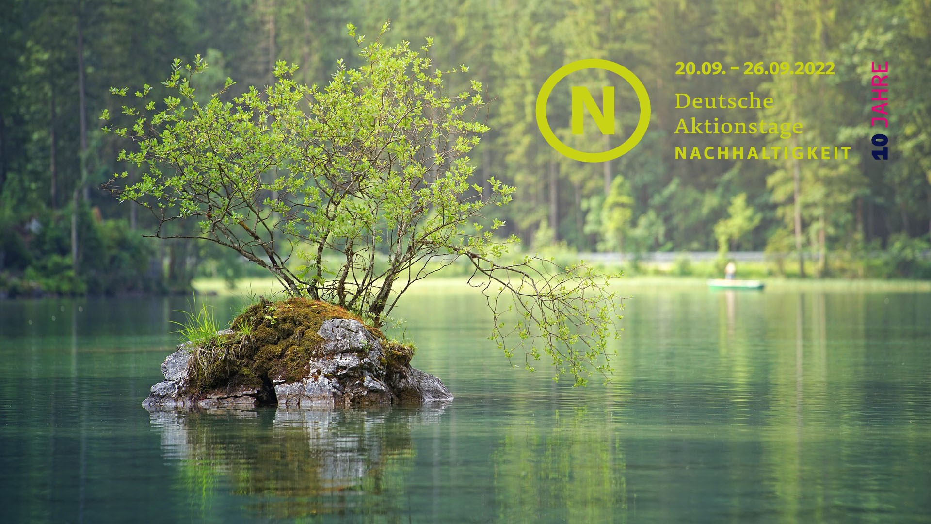 In einem See steht eine kleine Insel, auf der ein Baum wächst, im Hintergrund ein Wald. In der Bildecke oben rechts steht das Logo der Deutschen Aktionstage für Nachhaltigkeit.
