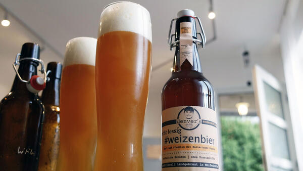 Neben einer Flasche mit Weizenbier stehen zwei volle Biergläser und zwei geöffnete Bierflaschen.