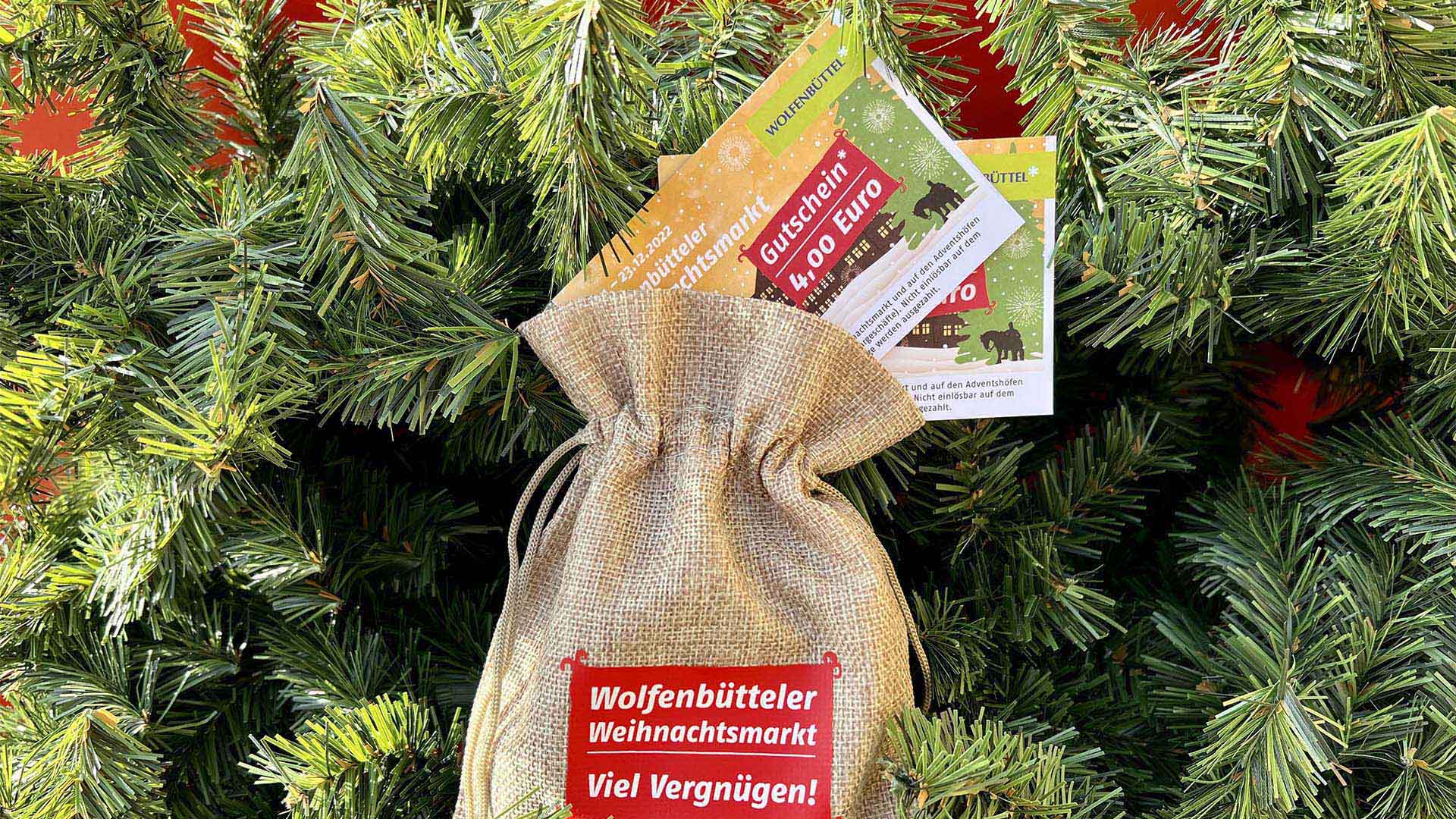 Auf einem Tannenzweig liegt ein Jutesäckchen mit Gutscheinen und der Aufschrift "Wolfenbütteler Weihnachtsmarkt - Viel Vergnügen!"