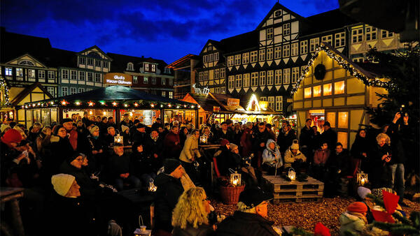 Publikum steht und sitzt vor der Bühne bei der Eröffnung des Weihnachtsmarktes, im Hintergrund Weihnachtsmarkt-Hütten und das Wolfenbütteler Rathaus
