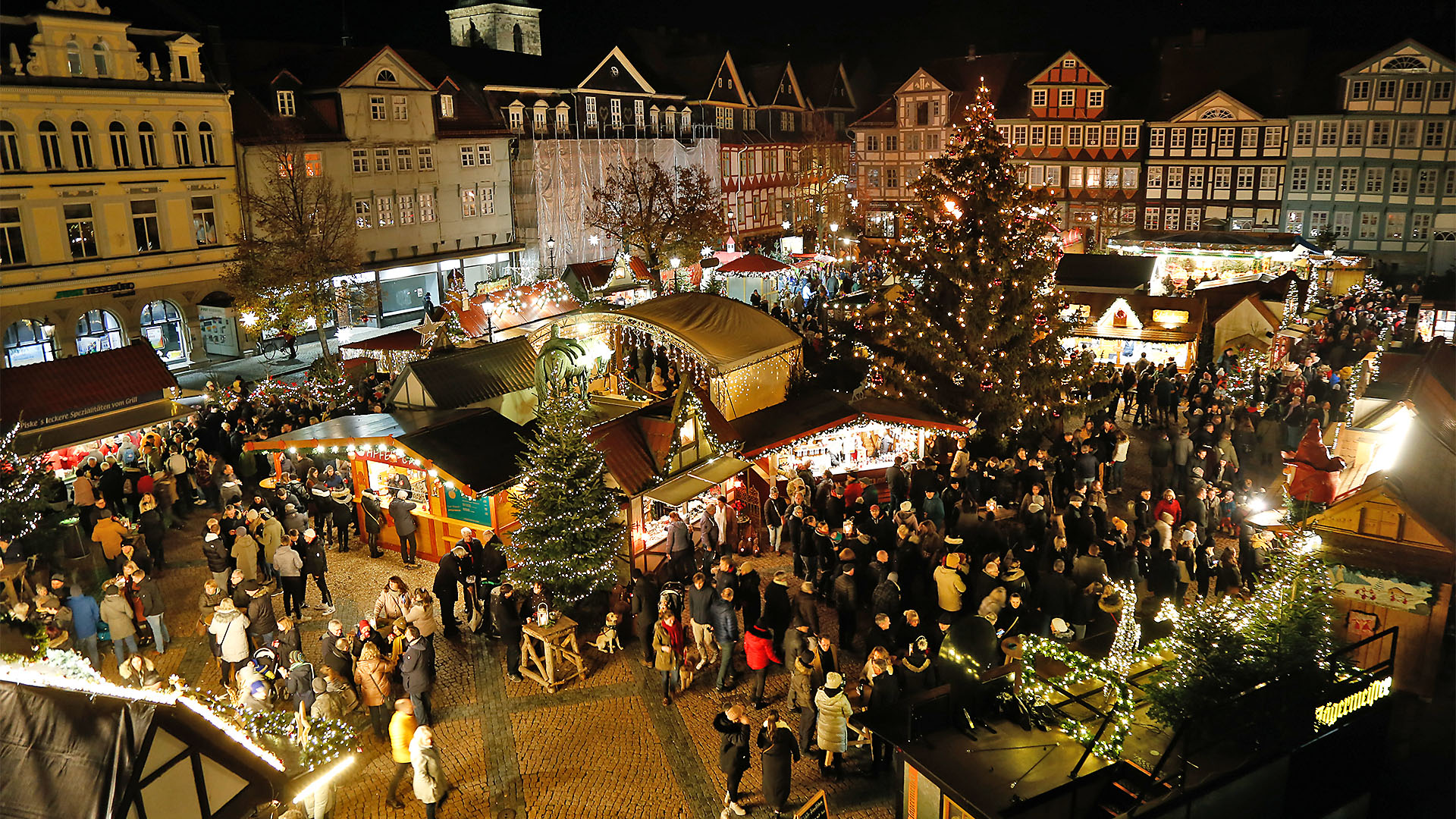 Blick auf den Weihnachtsmarkt mit dne beleuchteten Verkaufsständen, einer großen beleuchteten Tanne und vielen Besucherinnen und Besuchern.
