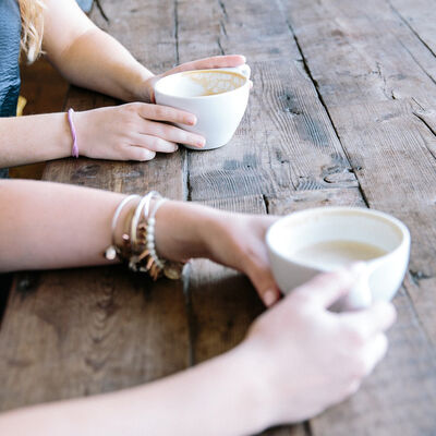 Zwei Paare Frauenhände halten je eine Kaffeetasse auf einem Holztisch