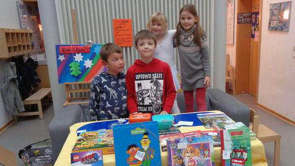 Kita-Kinder stehen um einen Tisch mit Büchern und Spielen.