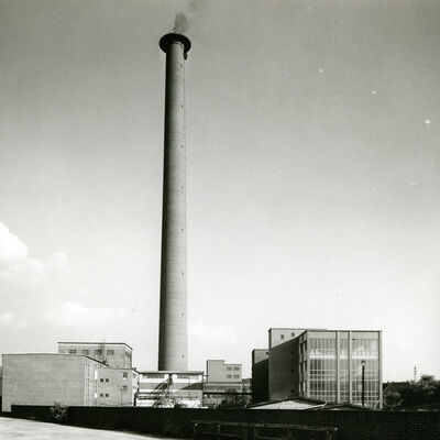 Außenansicht eines FAbrikgebäudes mit sehr hohem Schornstein. Schwarzweiß-Aufnahme