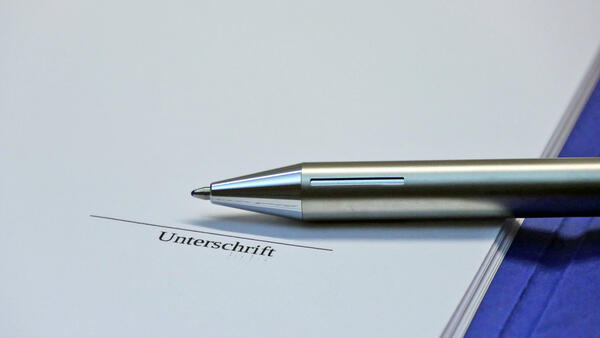 Ein Kugelschreiber liegt auf einem Blatt Papier, auf dem ein Bereich mit dem Vermerk "Unterschrift" markiert wurde.