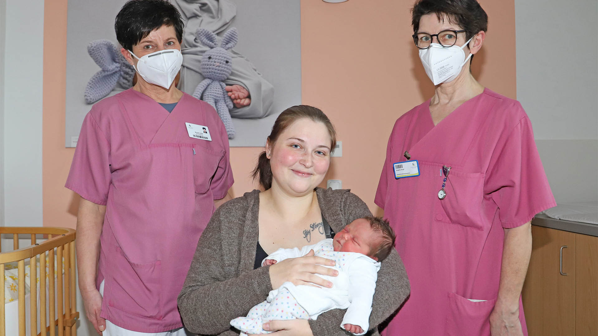 Zwischen zwei Krankenschwestern sitzt eine Frau mit einem Baby im Arm.