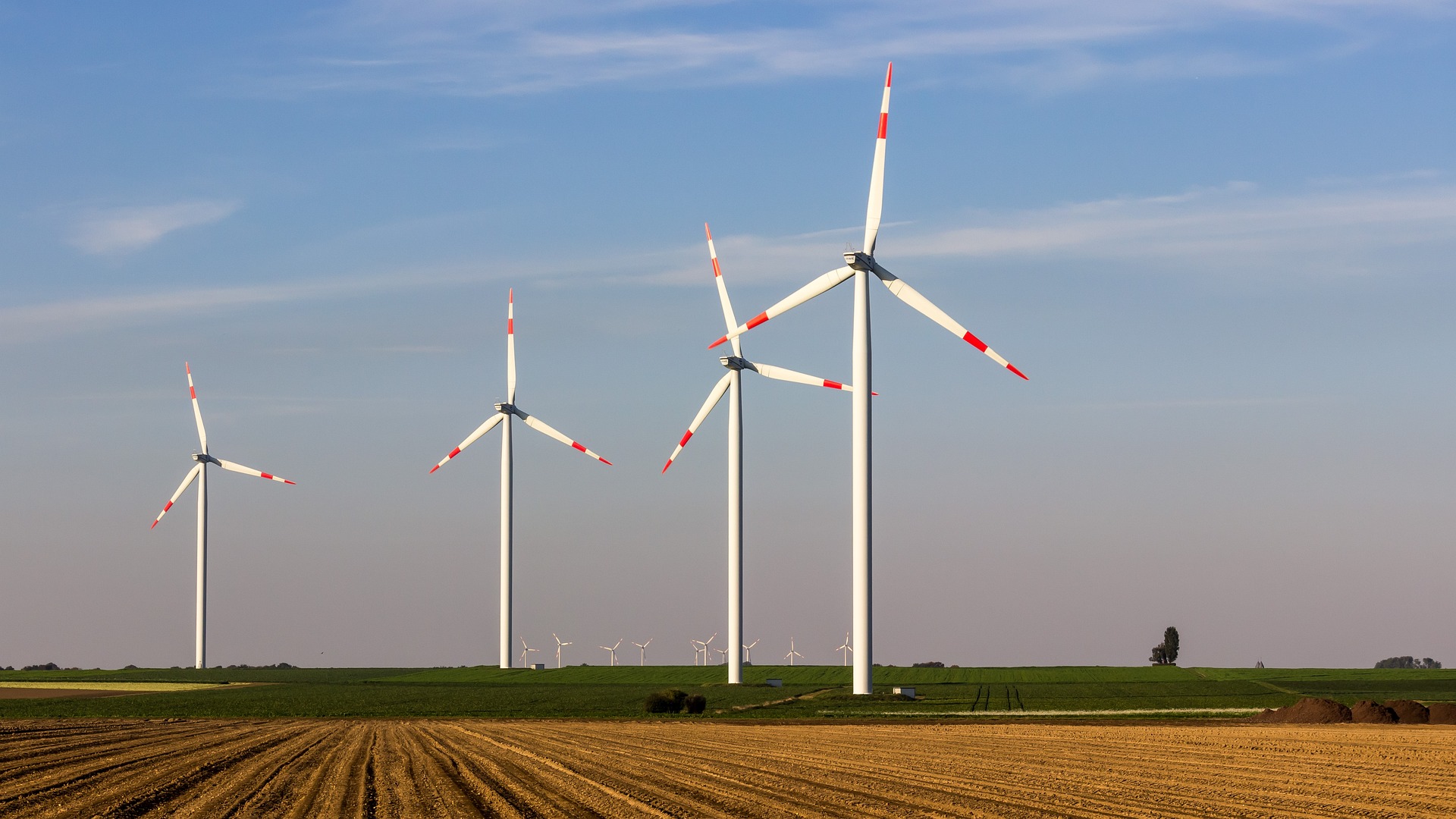 Hinter einem Stoppelfeld sieht man eine Windkraftanlage aus vier Windrädern und mehreren Windrädern in weiterer Entfernung.