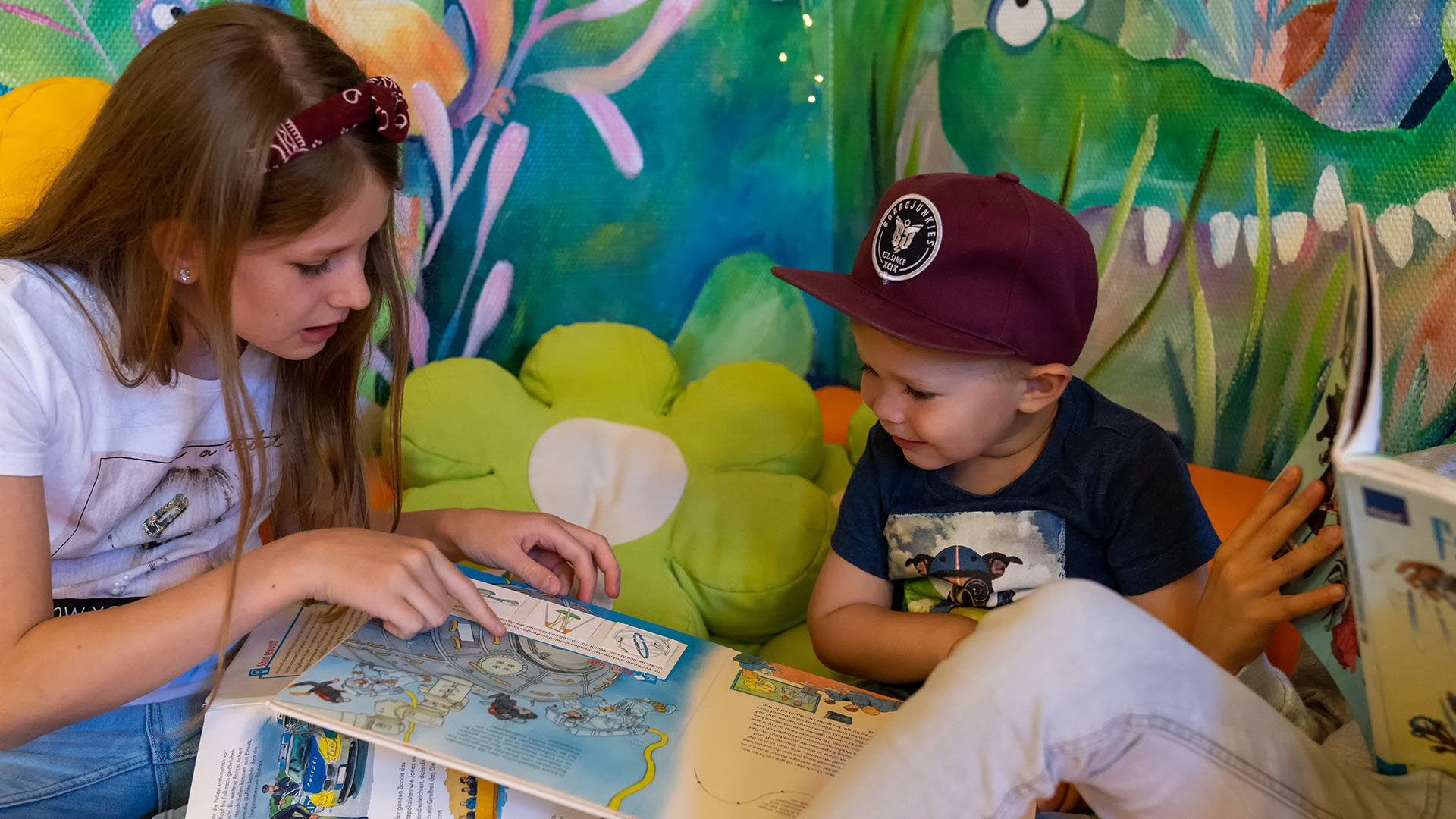 Ein  Mädchen und ein kleinerer Junge lesen gemeinsam in der Stadtbücherei in einem Buch.