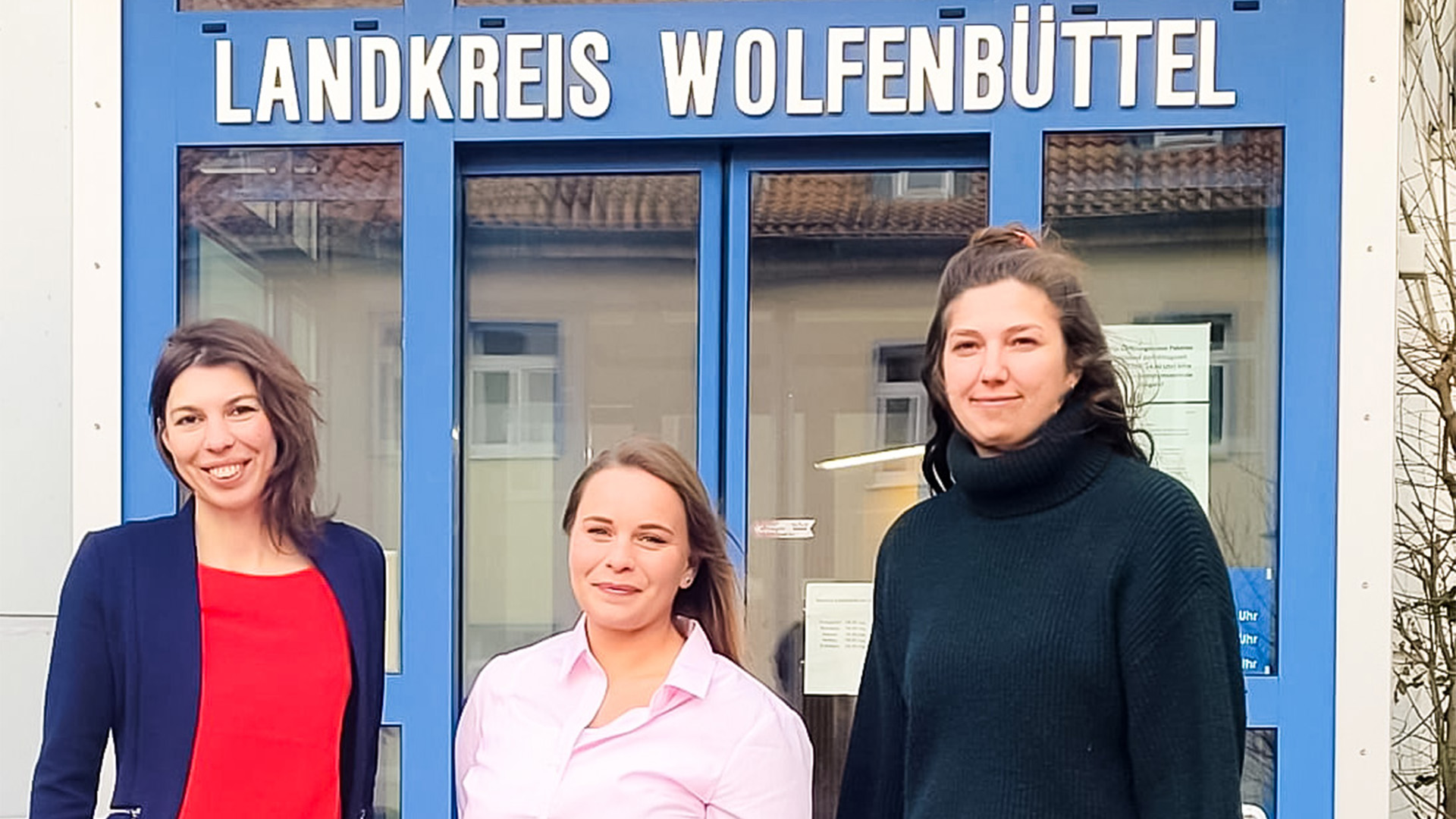 Drei Frauen stehen vor der Eingangstür des Landkreises Wolfenbüttel, dessen Schriftzug über der Tür zu erkennen ist.