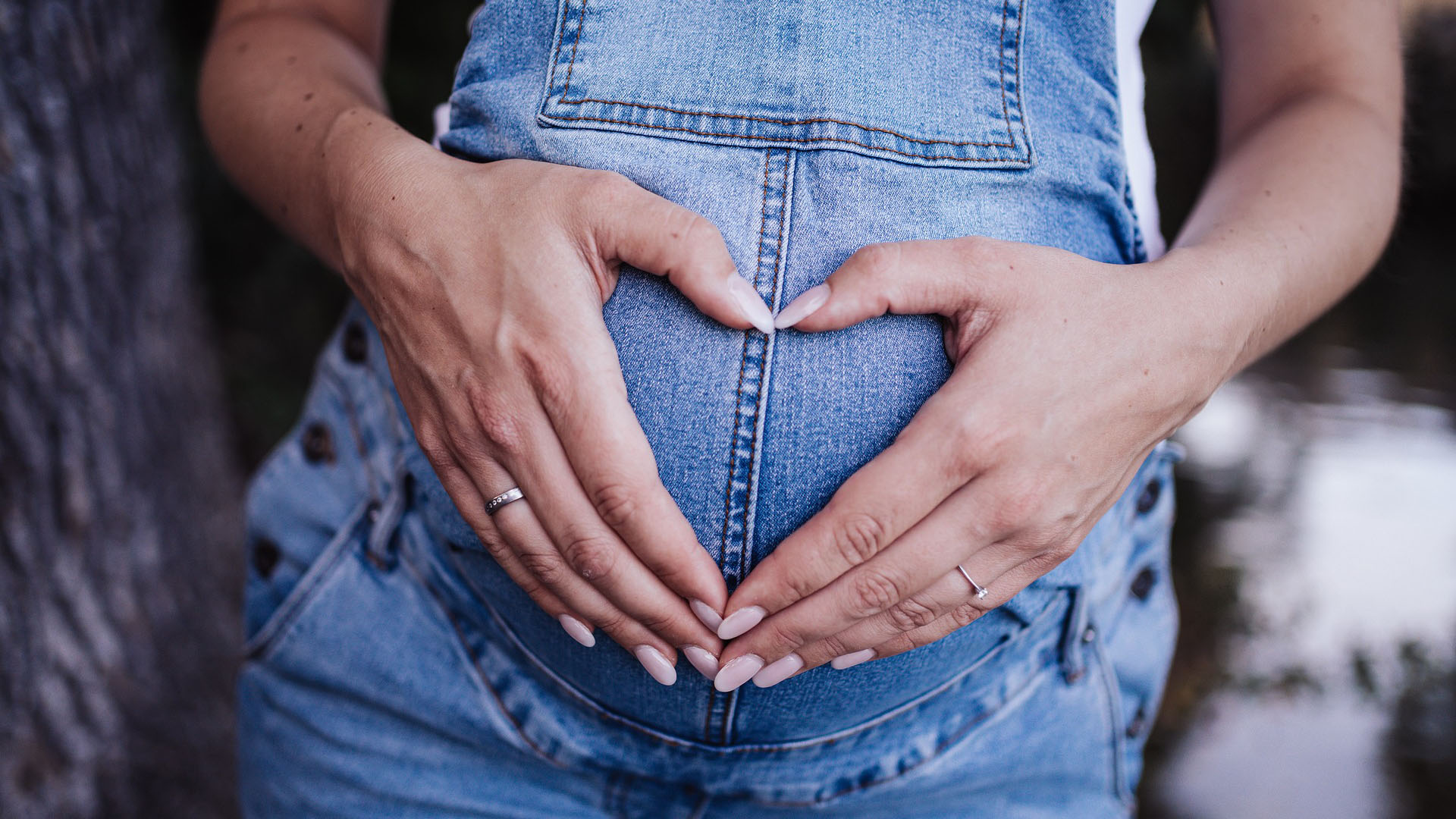 Eine Schwangere hält ihre Hände - zusammengelegt in Hrzform - auf ihren Schwangerschaftsbauch, man sieht nur die Hände und den Bauch.