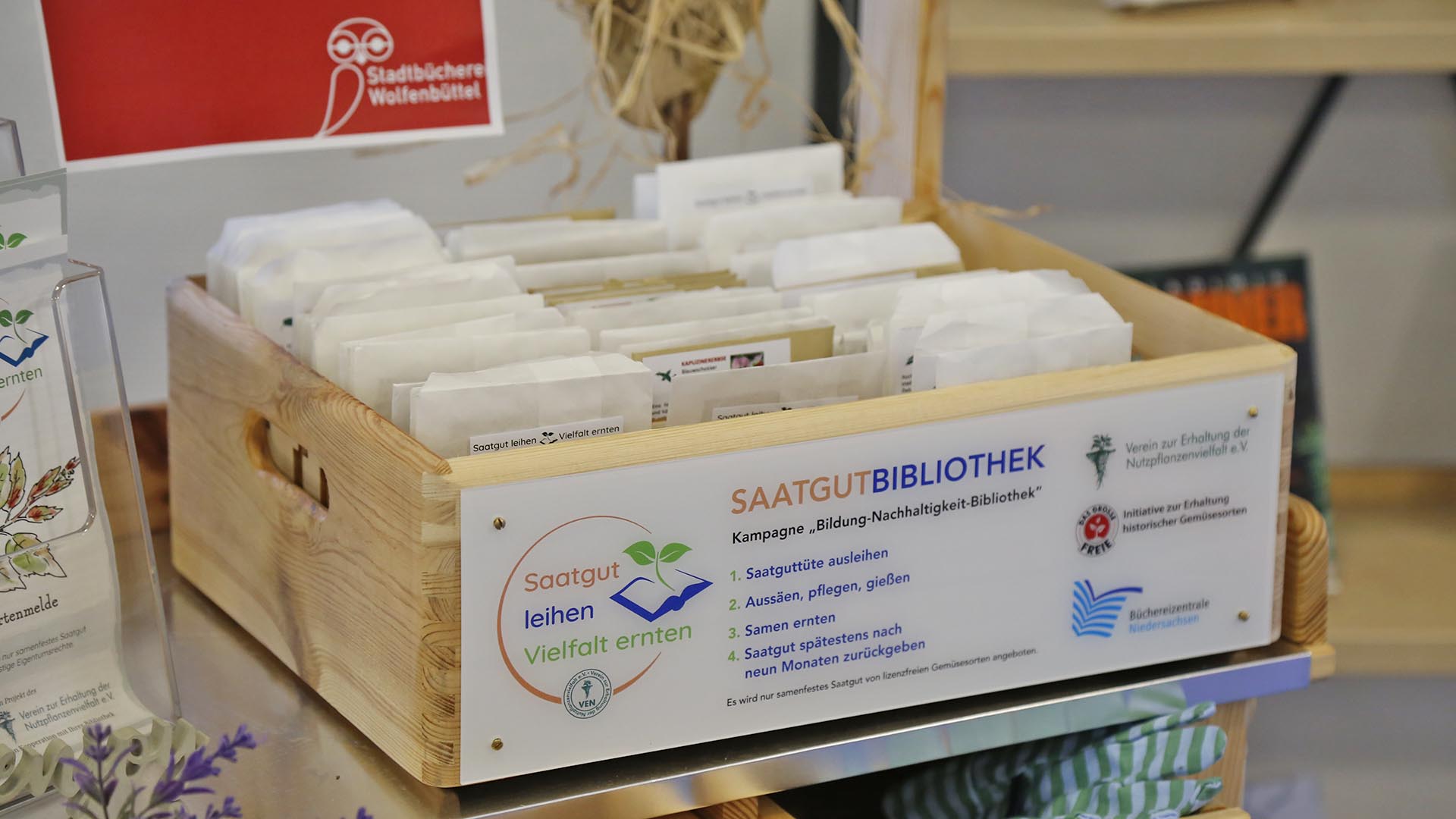 In einer Holzkiste stehen verschiedene braune Papiertütchen mit Saatgut, auf der Kiste steht "Saatgutbibliothek".