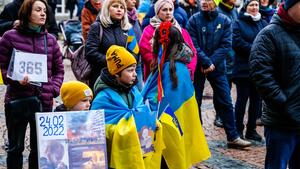 Viele Erwachsene und Kinder mit Bannern und ukrainischen Flaggen stehen auf dem Stadtmarkt.