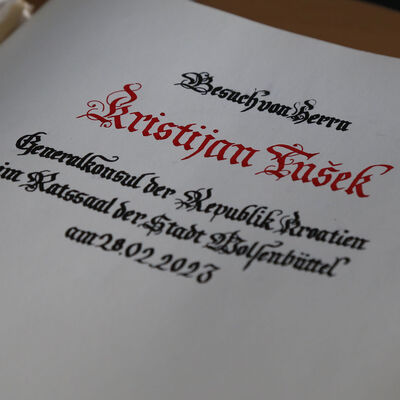 Auf einer weißen Buchseite aus festem Papier steht in verschnörkelten Buchstaben "Besuch von Herrn Kristijan Tušek - Generalkonsul der Republik Kroatien im Ratssaal der Stadt Wolfenbüttel am 28.02.2023