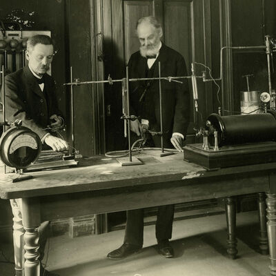 Schwarzweißfoto von Julius Elster und Hans Friedrich Geitel mit Versuchsaufbau an einem großen Holztisch