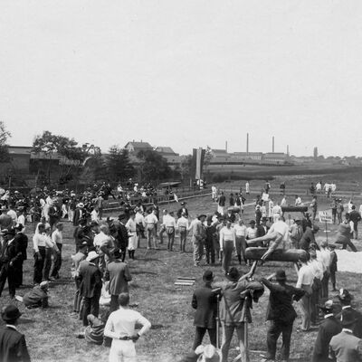 Schwarzweißfoto des Turnfestes des MTV Wolfenbüttel 1910, Menschen machen auf einer Wiese Geräteturnen am Barren oder Reck...