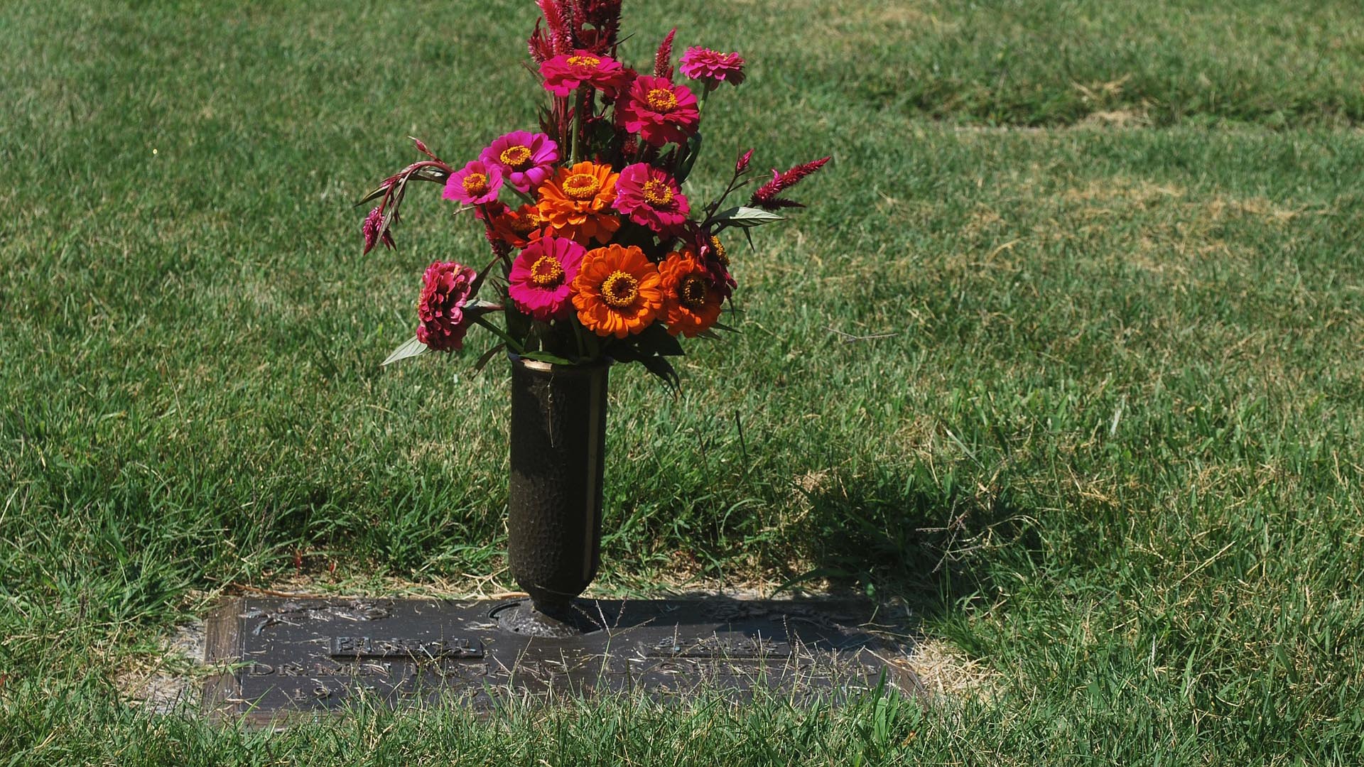 In eine Rasenfläche ist eine Grabplatte eingelassen, daneben steht eine Vase mit Blumenschmuck