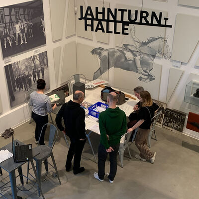 Blick von oben in das Bürger Museum: in der Ausstellung stehen fünf Personen an einem Tisch und scheinen über Ausstellungsexponate zu beraten.