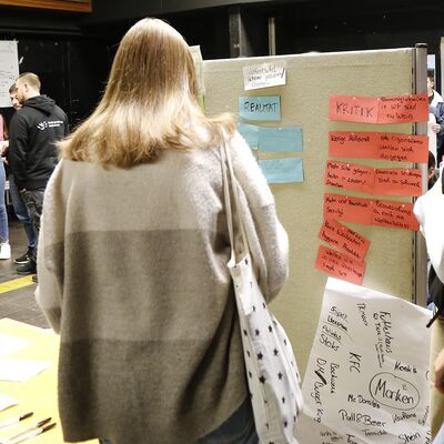 Eine junge Frau schaut sich eine Pinnwand mit verschiedenen Vorschlägen der Jugendlichen an.