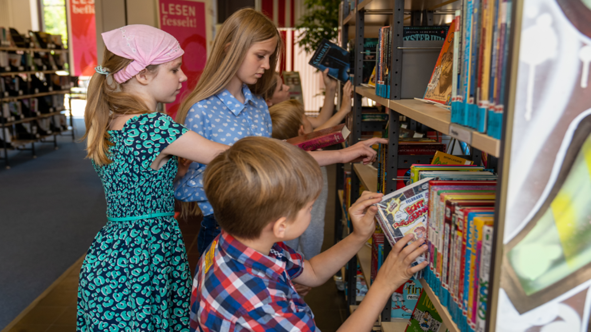 Drei Kinder stehen vor einem Bücherregal und suchen nach Büchern.