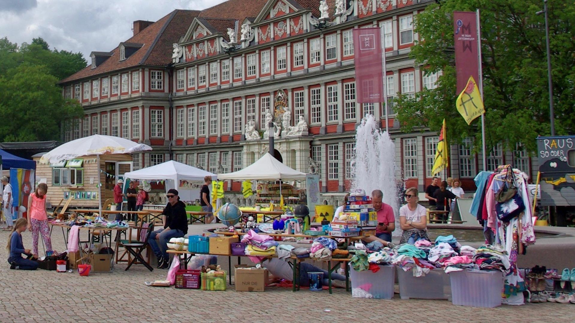 Auf einem Platz vor dem Wolfenbütteler Schloss, dessen Fassade im Hintergrund zu sehen ist, stehen einige Flohmarktstände mit angebotenen Gebrauchtwaren wie Kleidungsstücken.