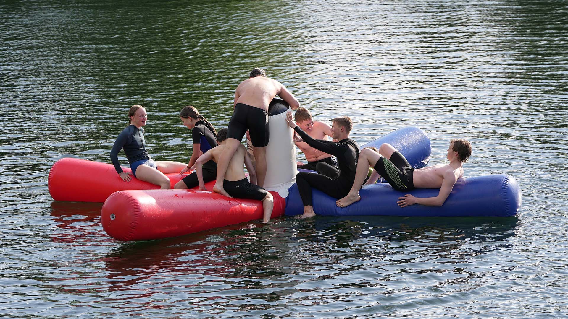 Inmitten eines Sees schwimmt ein aufgeblasenes Wasserspielgerät, die sogenannte Krake, auf dem sich Jugendliche befinden.