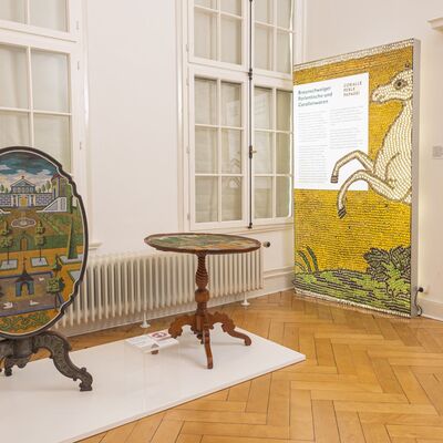 Ausstellungsraum mit perlenbesetzten Tischplatten und Ausstellungstafel