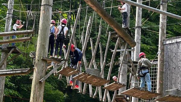 Jugendliche mit Helm und Gurtgeschirr klettern in einem Hochseilgarten über Hängebrücken